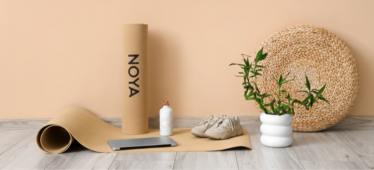Yoga mat with 'NOYA' branding on a wooden floor against a beige wall.