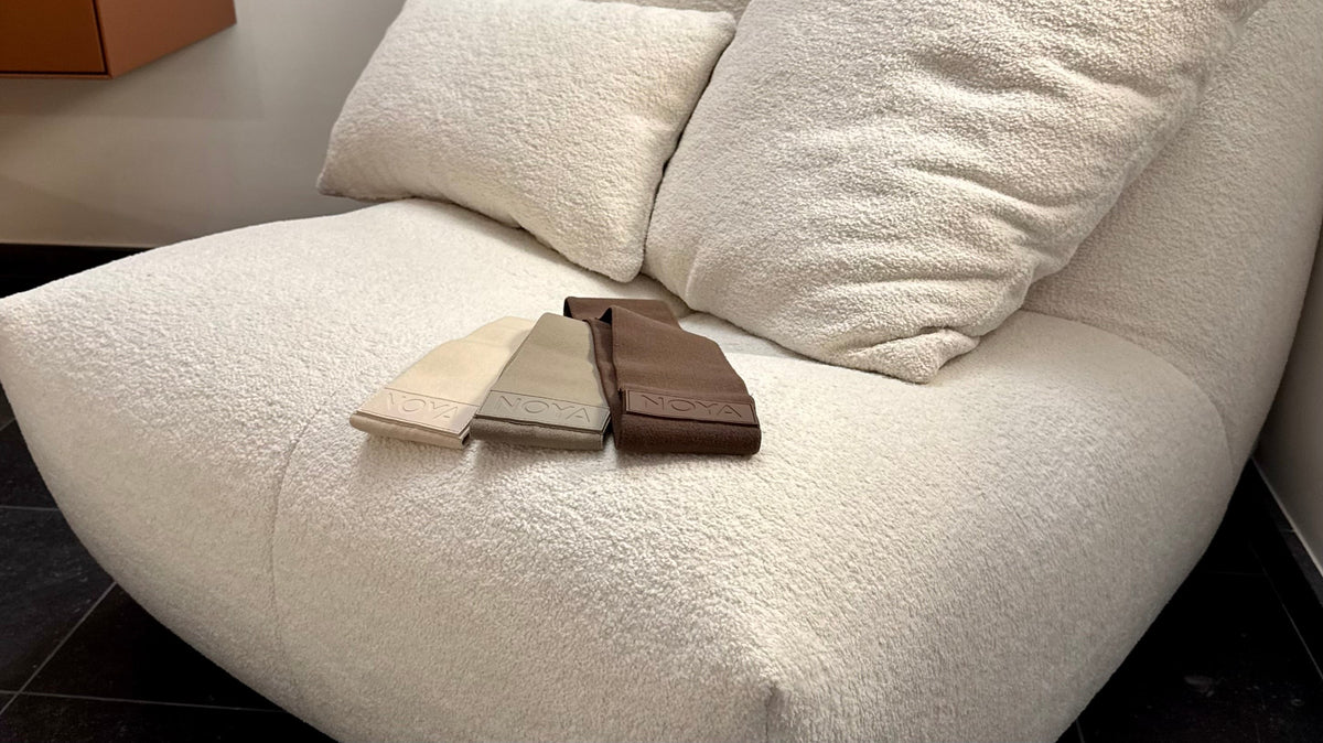 NOYA Resistance Trio: tres bandas elásticas de tela para cadera en tonos naturales sobre un sillón crema suave; accesorios minimalistas de gimnasio en casa para el movimiento consciente y el entrenamiento con el propio peso.